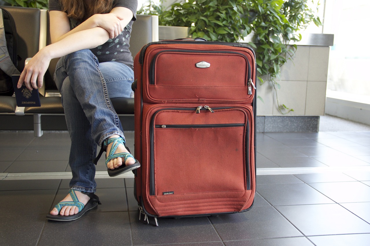 Kobieta siedząca na lotnisku z wielką czerwoną podróżną walizką obok